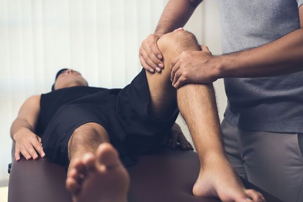 A Physician Examining A Patient’s Knee As The Patient Lays Down